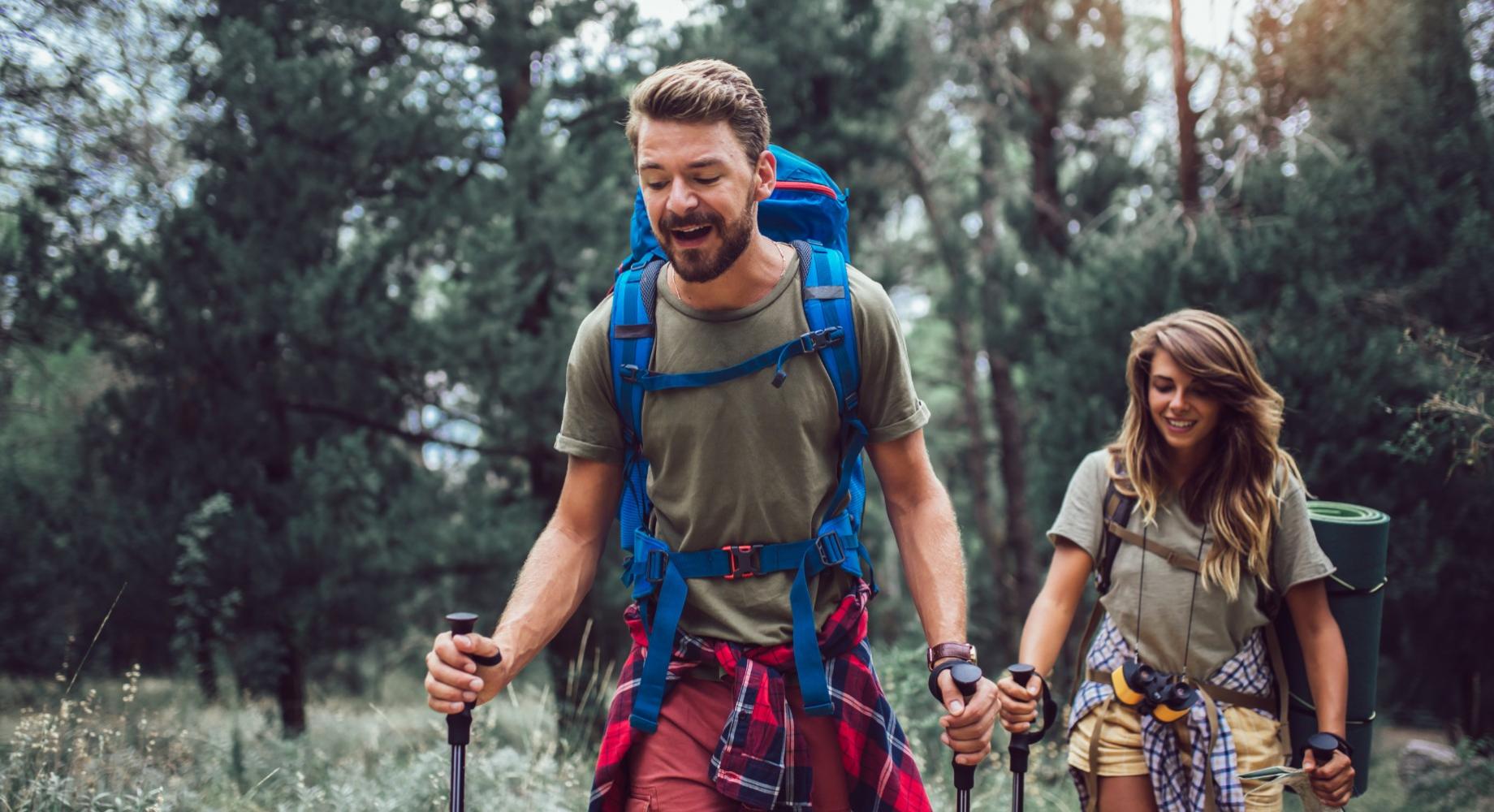 Coppia felice fa trekking nella foresta con zaini e bastoncini da trekking.