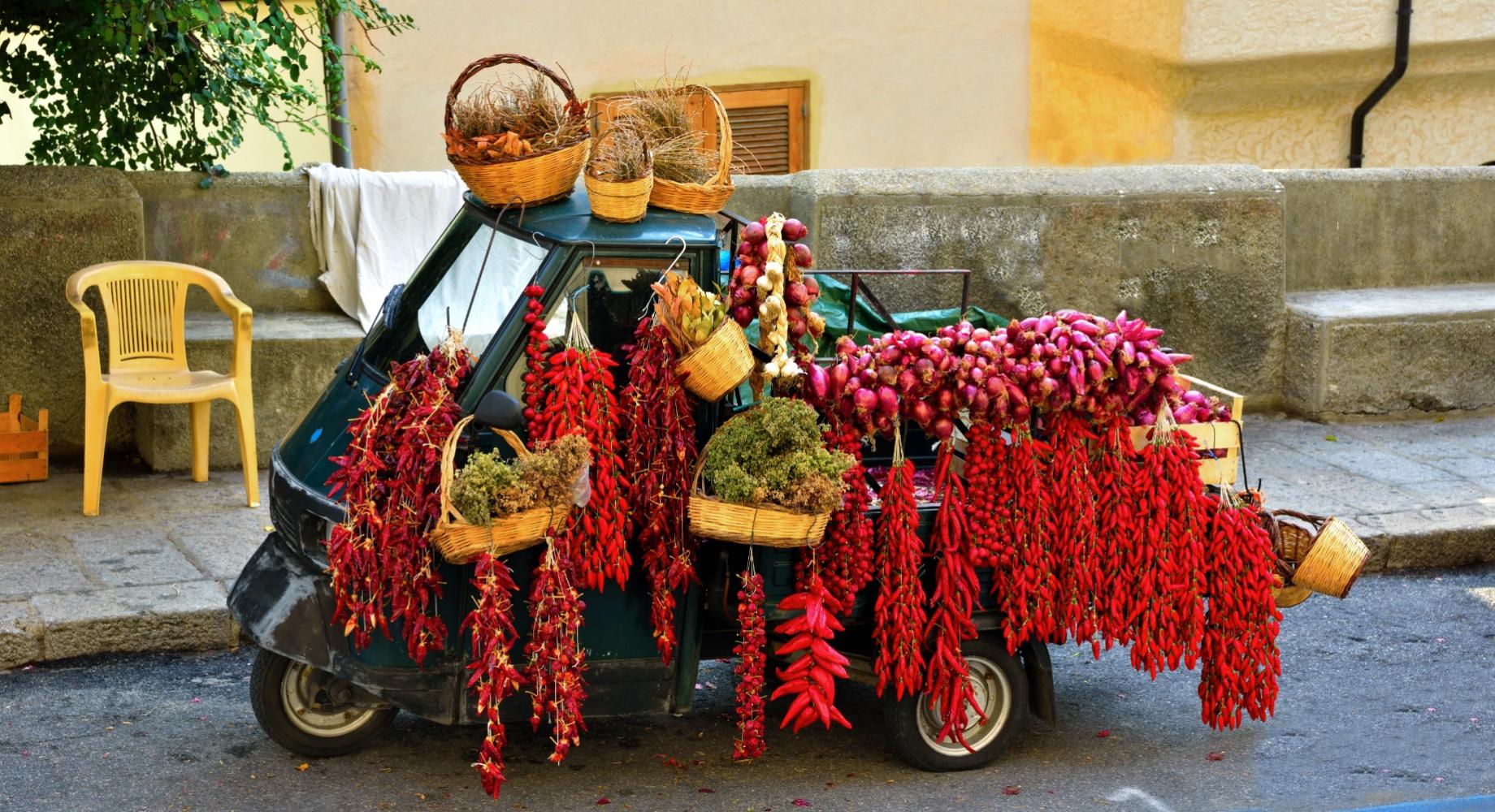 Ape car carica di peperoncini e cipolle rosse in una strada italiana.