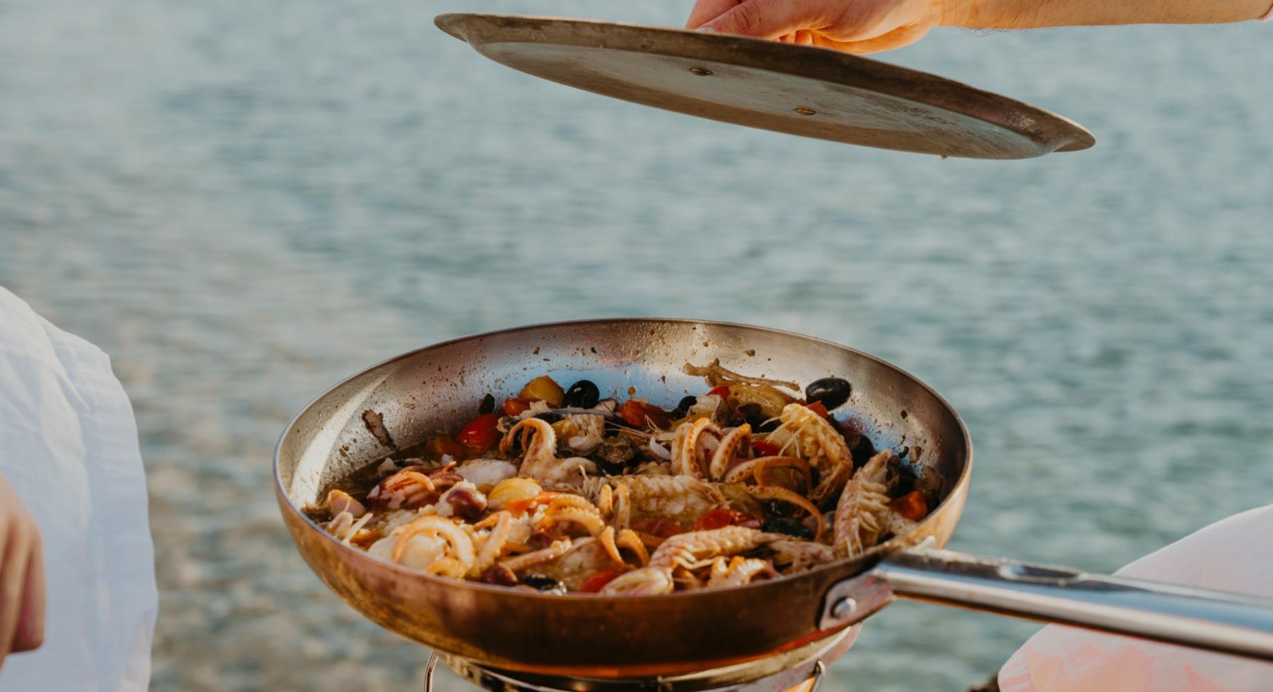 Cucina all'aperto: padella con frutti di mare e verdure vicino al mare.