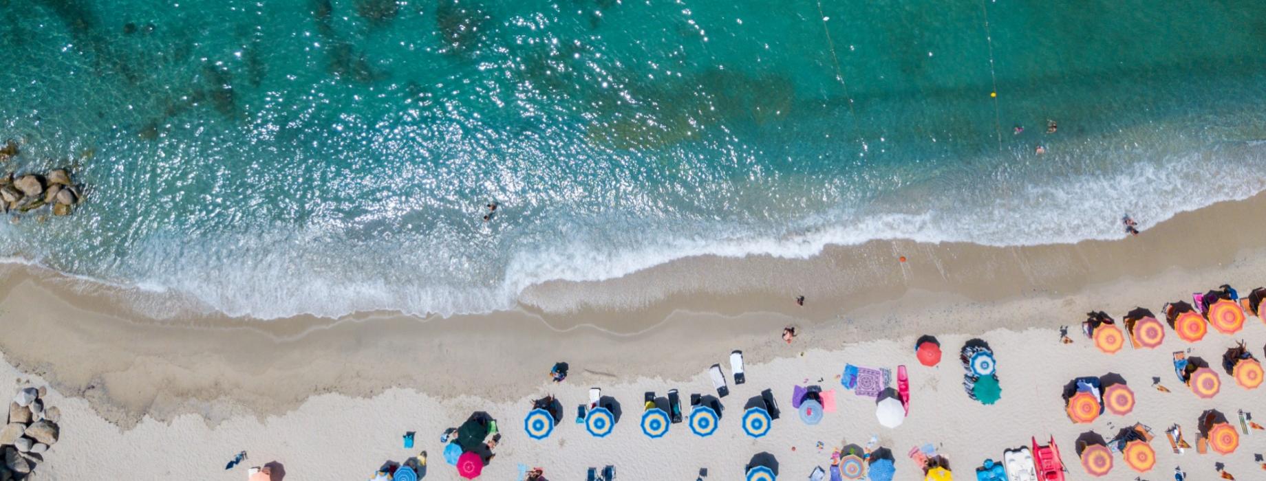 Spiaggia con ombrelloni colorati e mare cristallino, vista dall'alto.