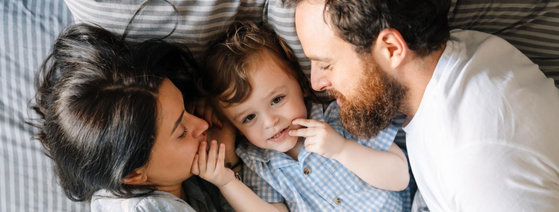 Una famiglia felice si abbraccia su un letto con lenzuola a righe.