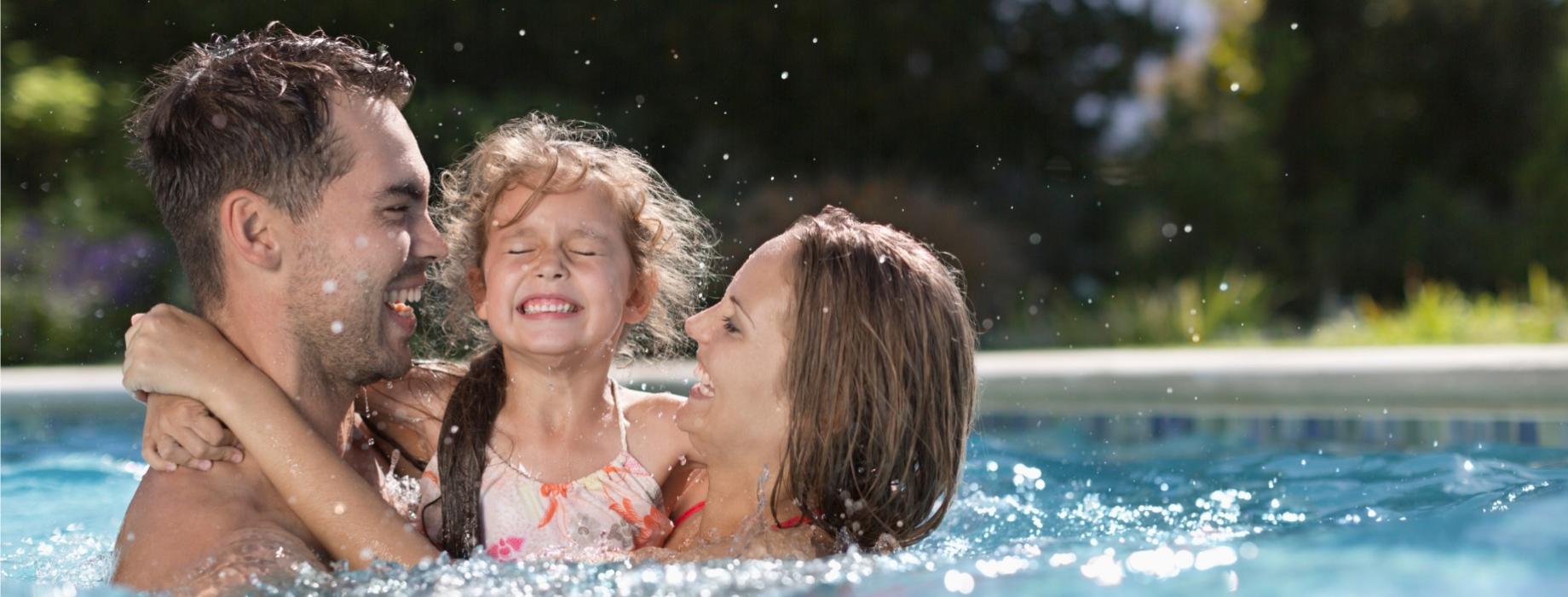 Famiglia felice che gioca in piscina, sorridendo e spruzzando acqua.