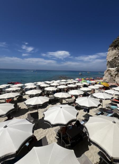 Spiaggia affollata con ombrelloni bianchi e mare azzurro sotto un cielo sereno.