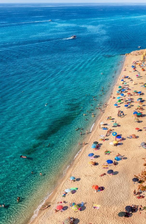 Spiaggia affollata con ombrelloni colorati e mare cristallino, vista dall'alto.