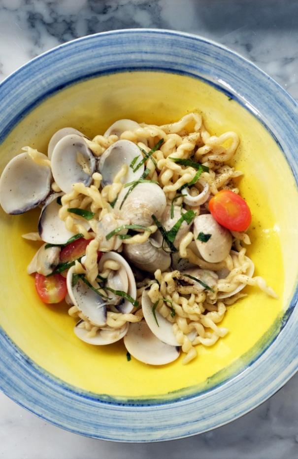 Pasta con vongole, pomodorini e prezzemolo in un piatto colorato.