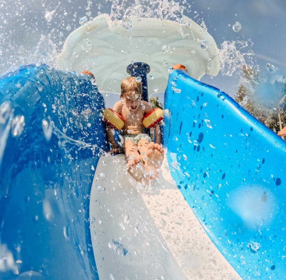 Bambino scivola su uno scivolo d'acqua, spruzzi ovunque, divertimento estivo.