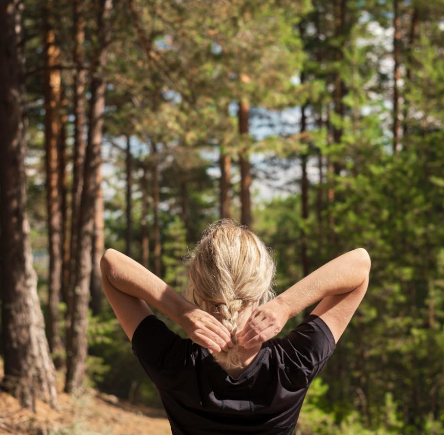 Persona in una foresta, sistema i capelli, circondata da alberi verdi.