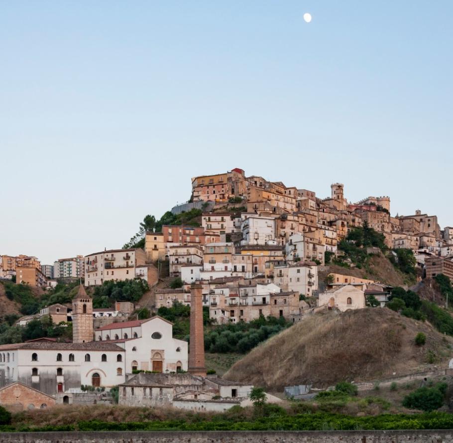 Paesaggio collinare con case storiche e una chiesa sotto la luna.