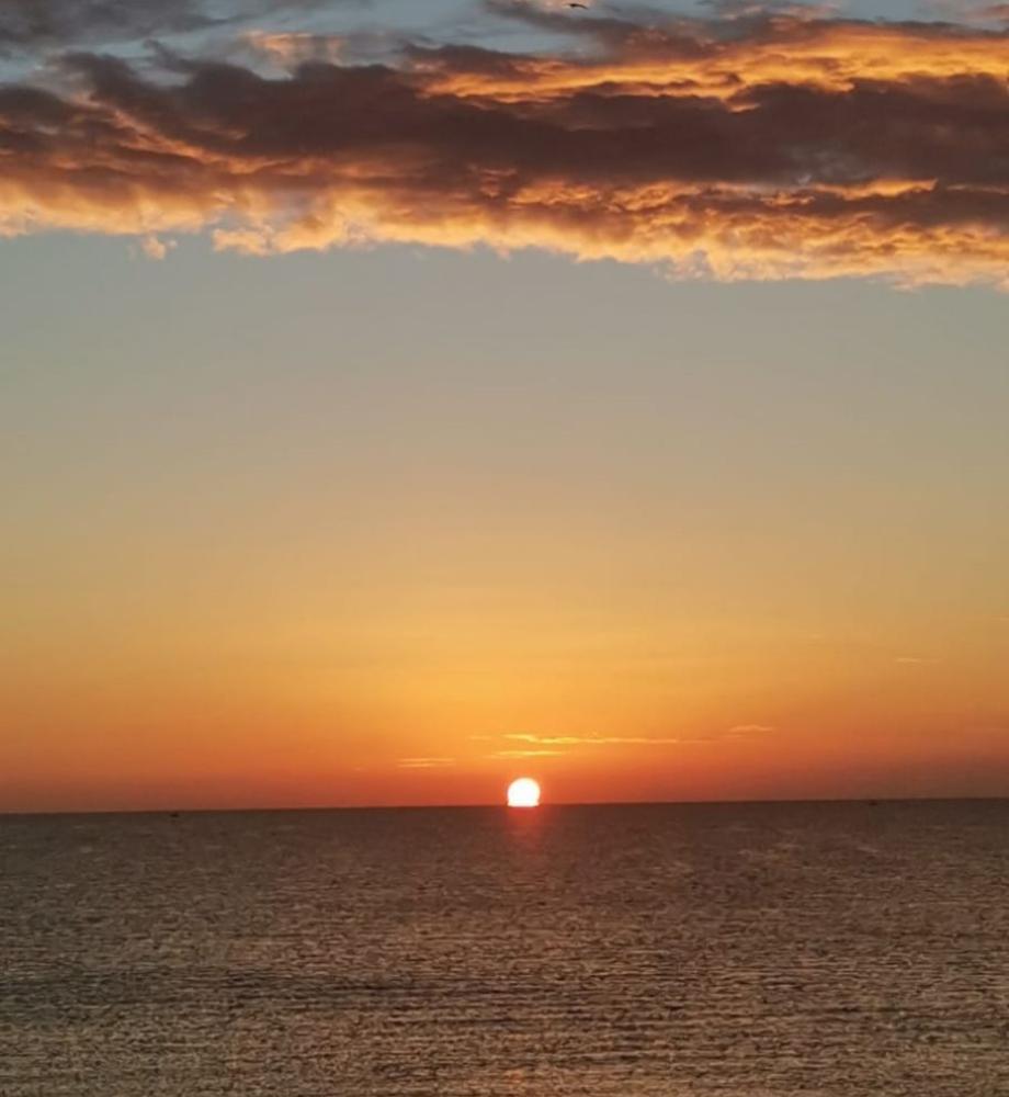 Spiaggia affollata con ombrelloni bianchi, mare blu e cielo sereno.