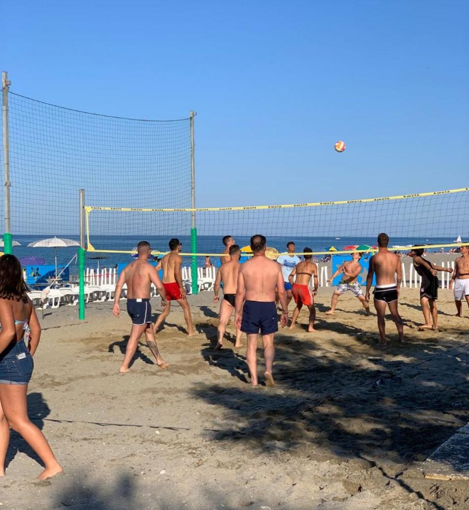 Partita di beach volley in corso su una spiaggia soleggiata con mare sullo sfondo.